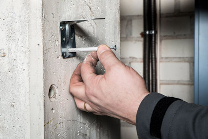 Hand placerar en spikplugg i ett byggbeslag mot betongvägg.